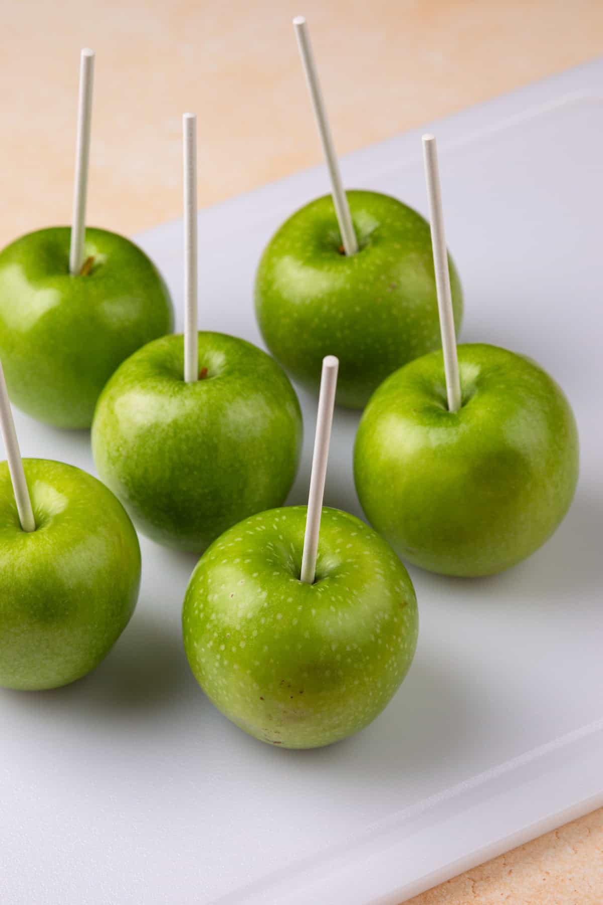 Six granny smith apples with candy sticks in them.