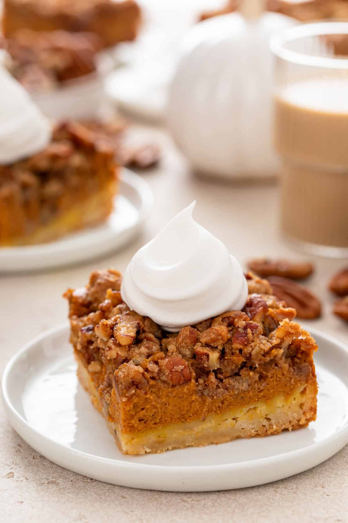 Pumpkin pecan pie bar on a white plate, topped with a dollop of whipped cream.