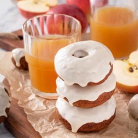 Three stacked apple cider donuts next to a glass of cider.