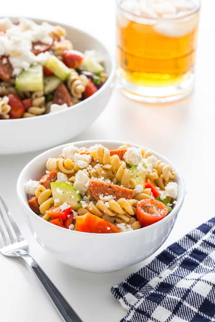 Small bowl of greek pasta salad with a larger serving bowl in the background