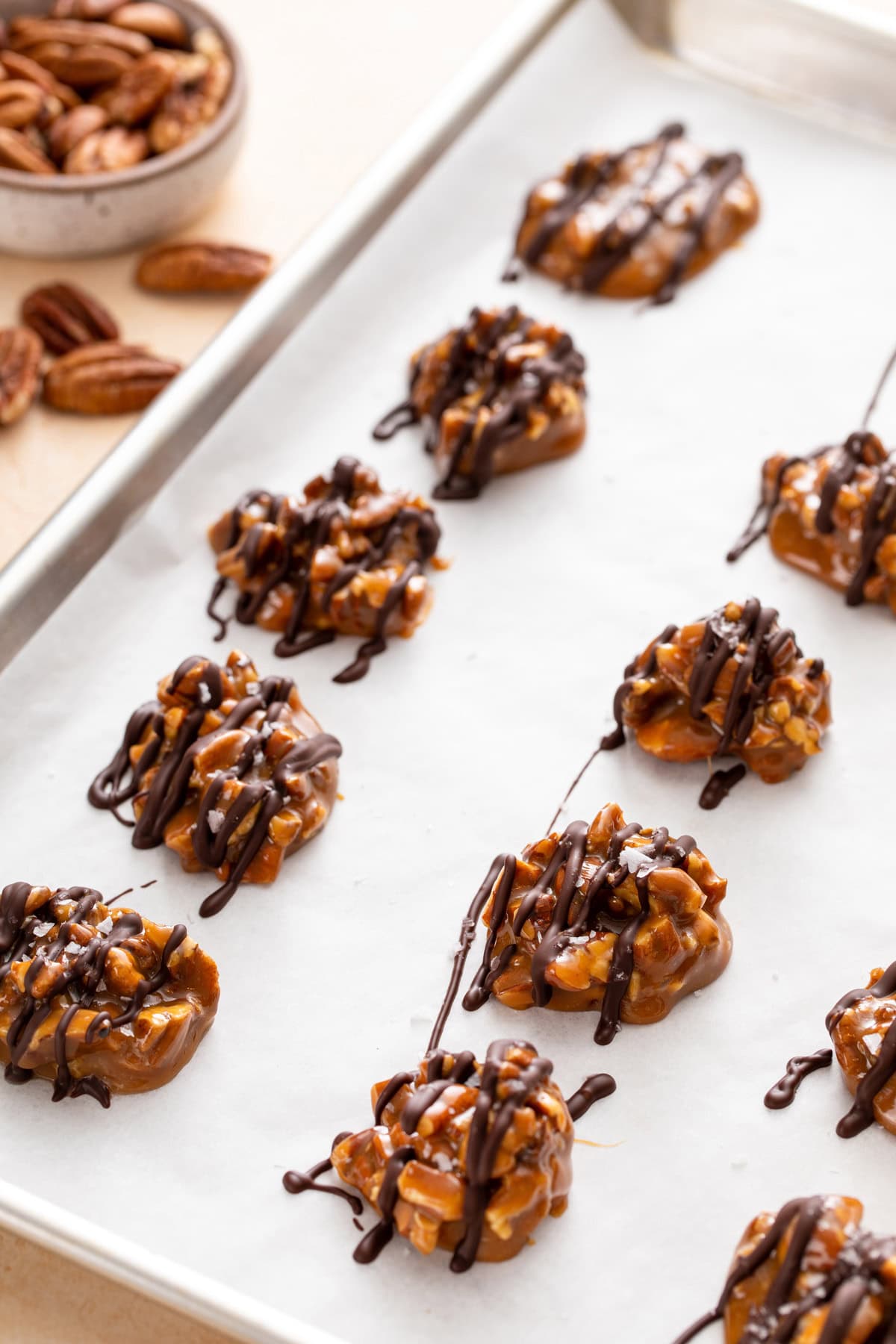 Chocolate drizzled on top of pecan caramel clusters on parchment paper.