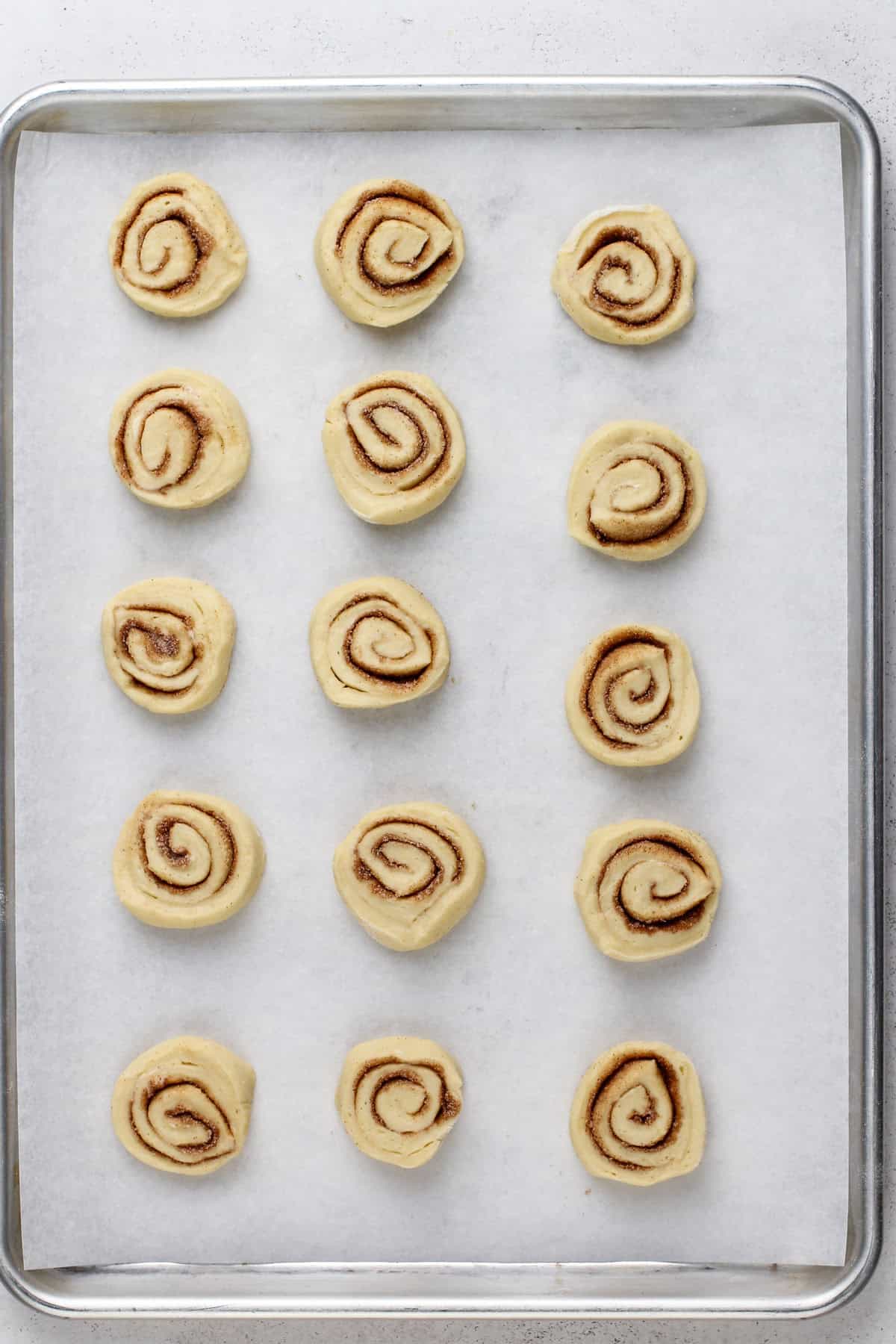 Sliced and unbaked mini cinnamon rolls on a sheet pan.