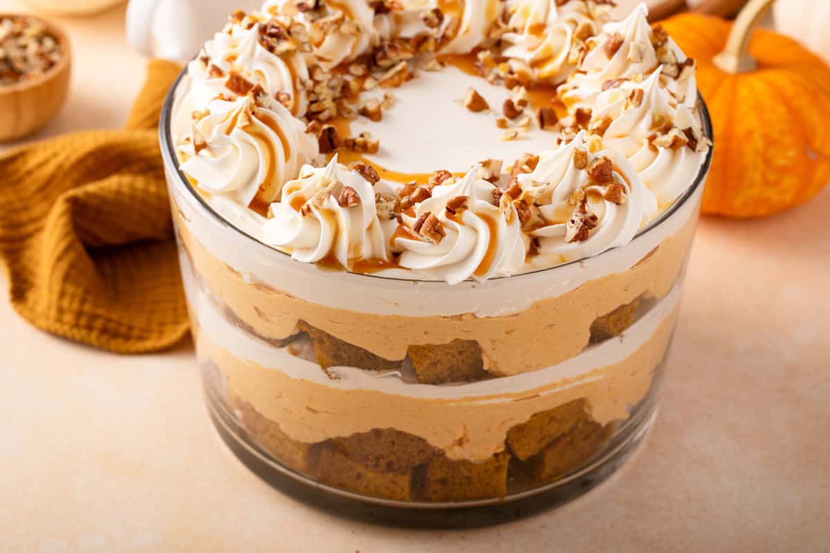 Pumpkin trifle in a trifle dish, garnished with chopped pecans and caramel sauce.