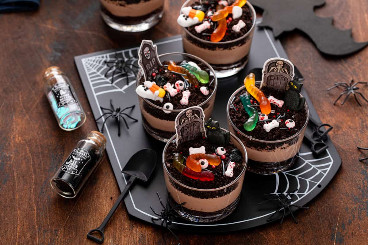 Four individual brownie dirt puddings, decorated with Halloween candies, arranged on a black platter.