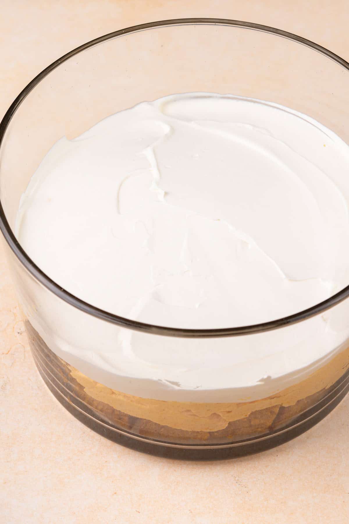 Whipped topping spread on top of pumpkin filling in a trifle dish.