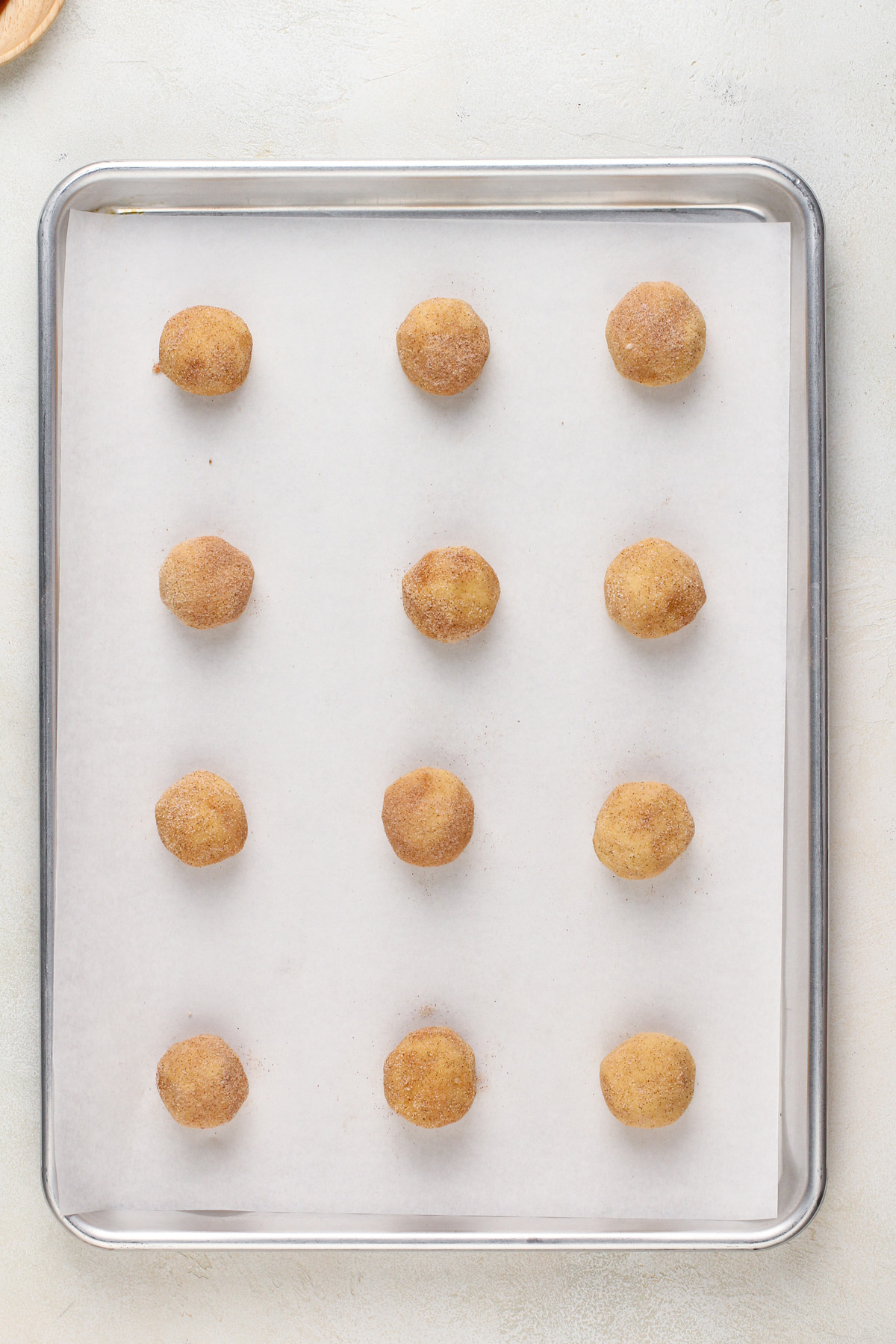 Unbaked snickerdoodle cookies on a parchment-lined baking sheet.