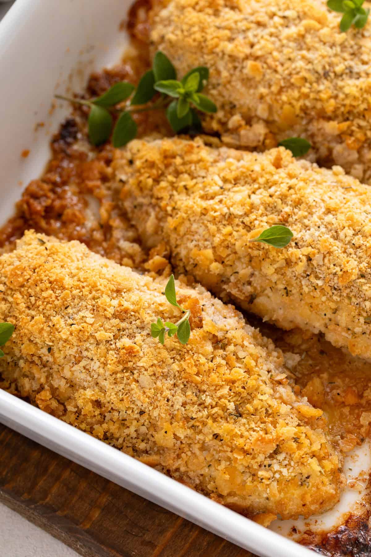 Close up of baked ritz cracker chicken in a white baking dish.