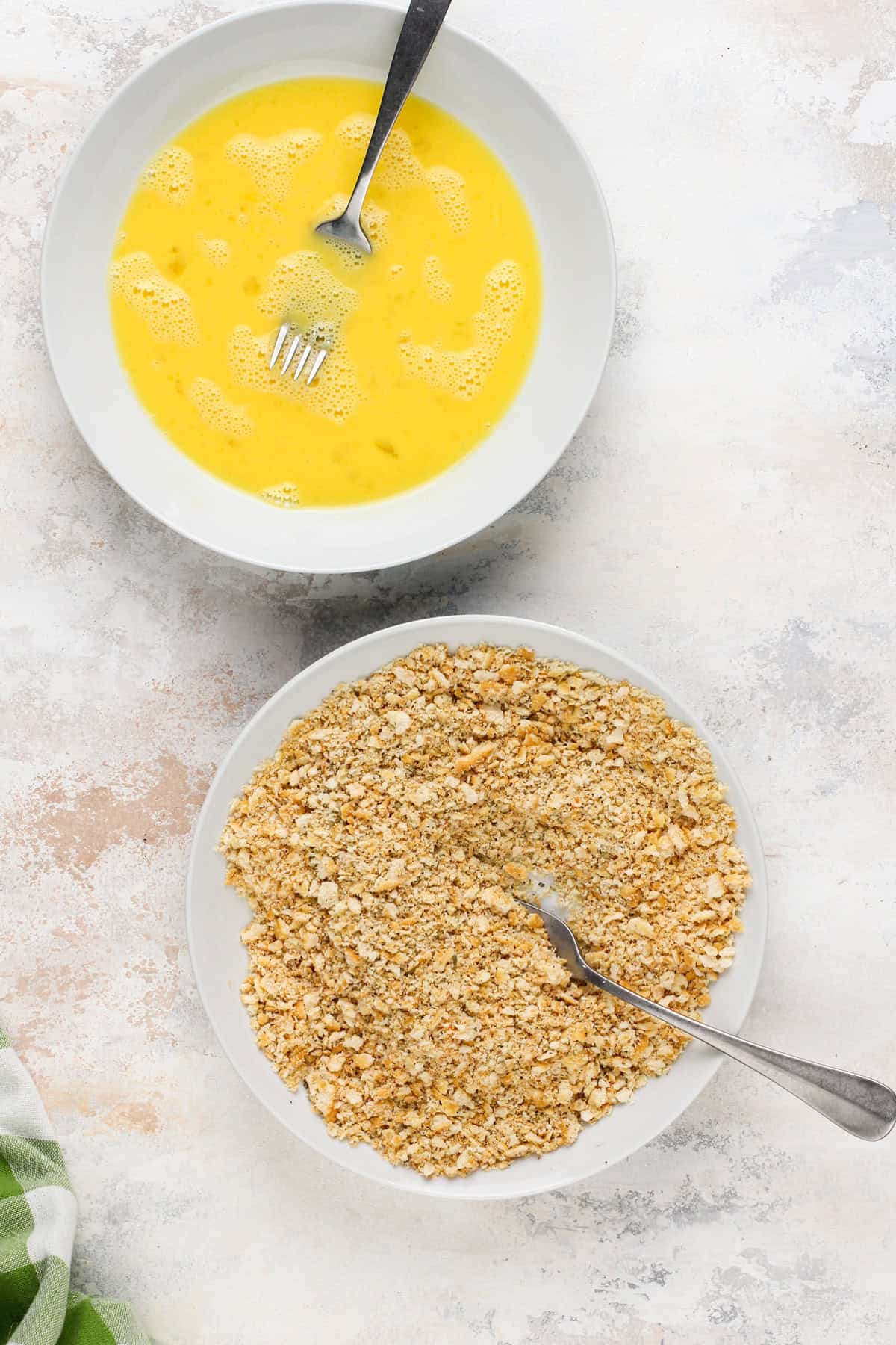 Two white bowls, one with whisked eggs and the other with seasoned ritz cracker crumbs in them.