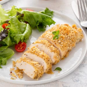 Sliced ritz cracker chicken next to salad on a white plate.