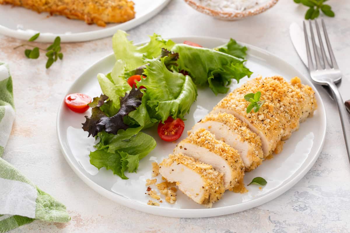 Sliced ritz cracker chicken arranged next to a side salad on a white plate.