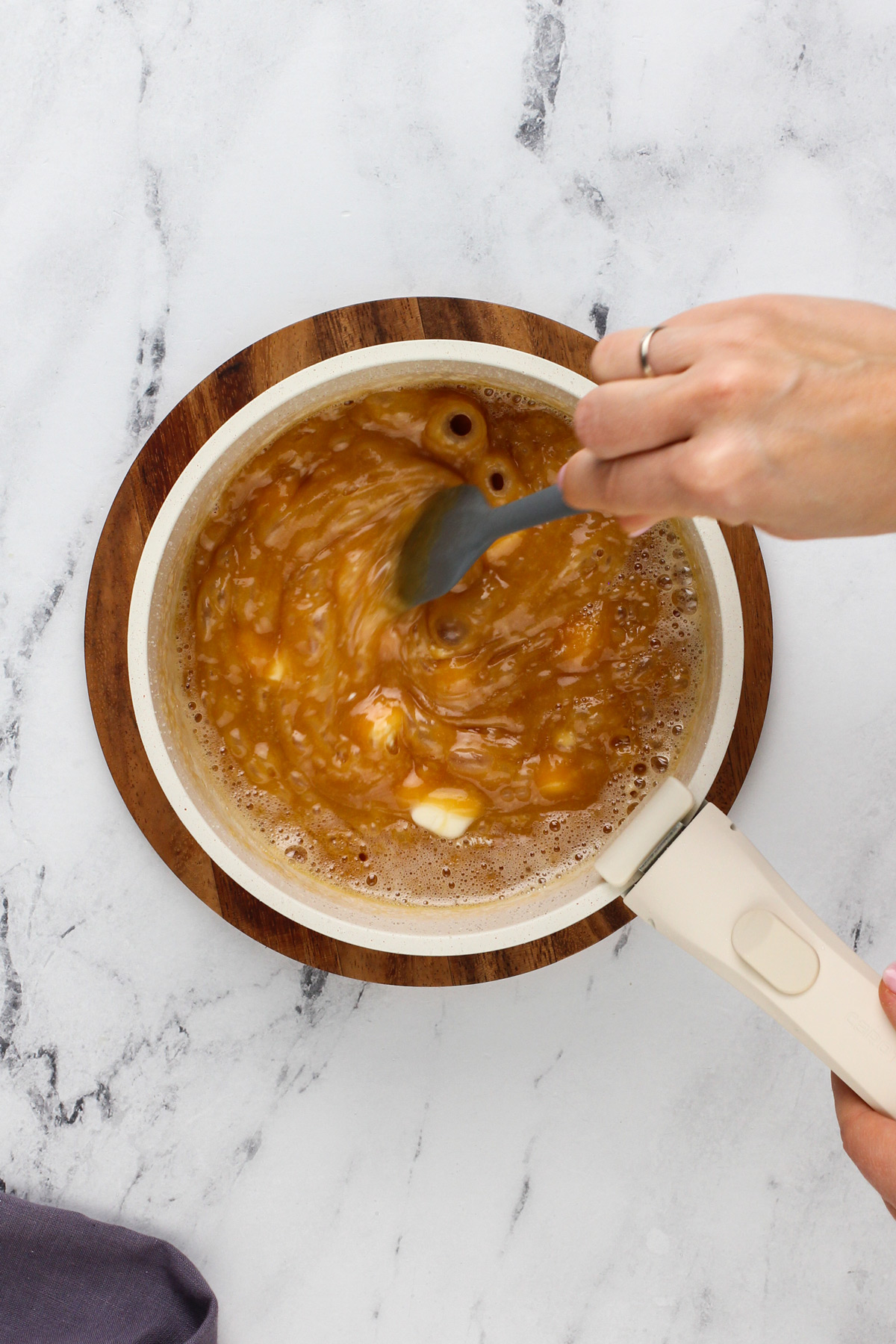 Hand stirring butter and cream cheese into caramel sauce.