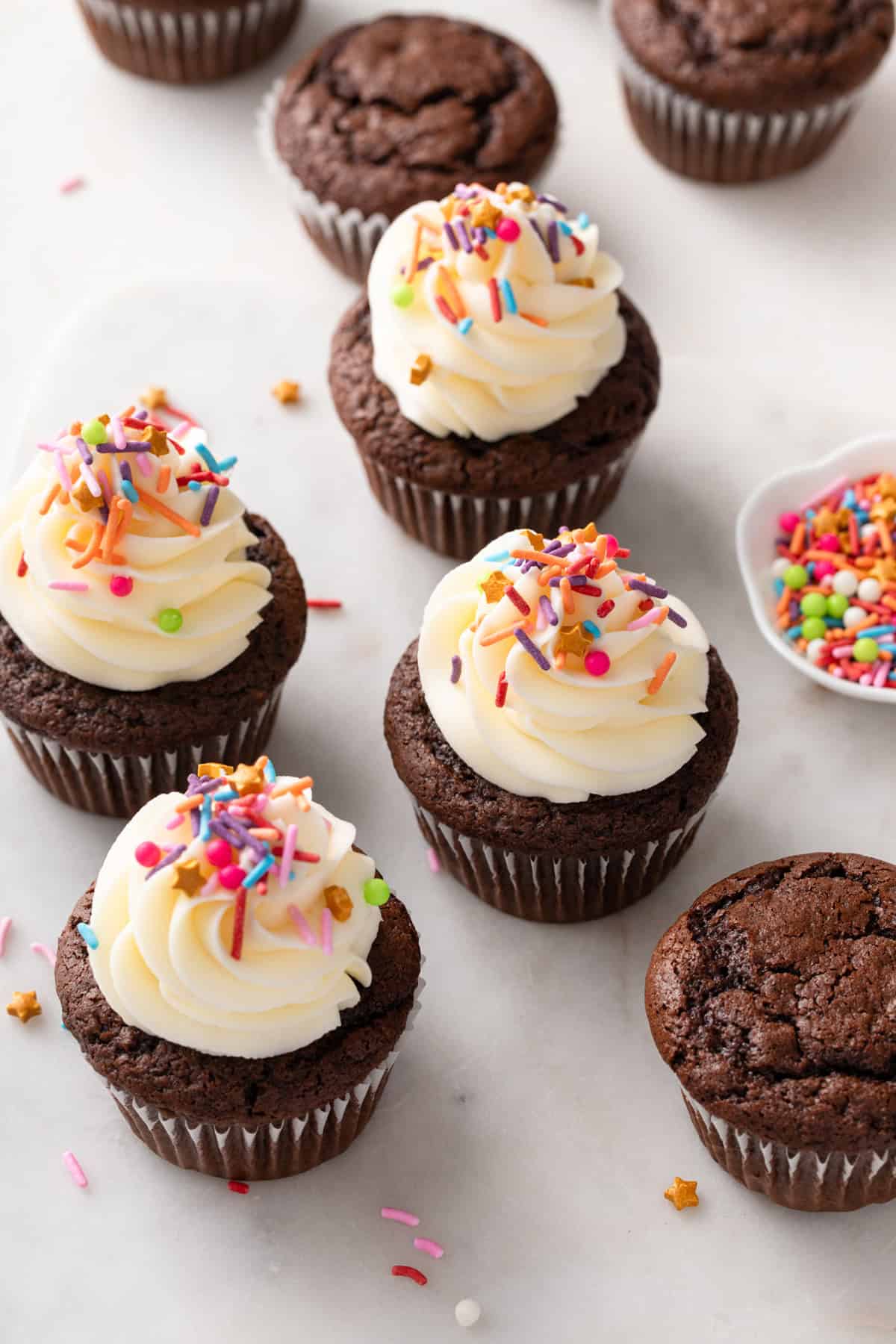 A mix of frosted and unfrosted chocolate cupcakes scattered on a countertop.