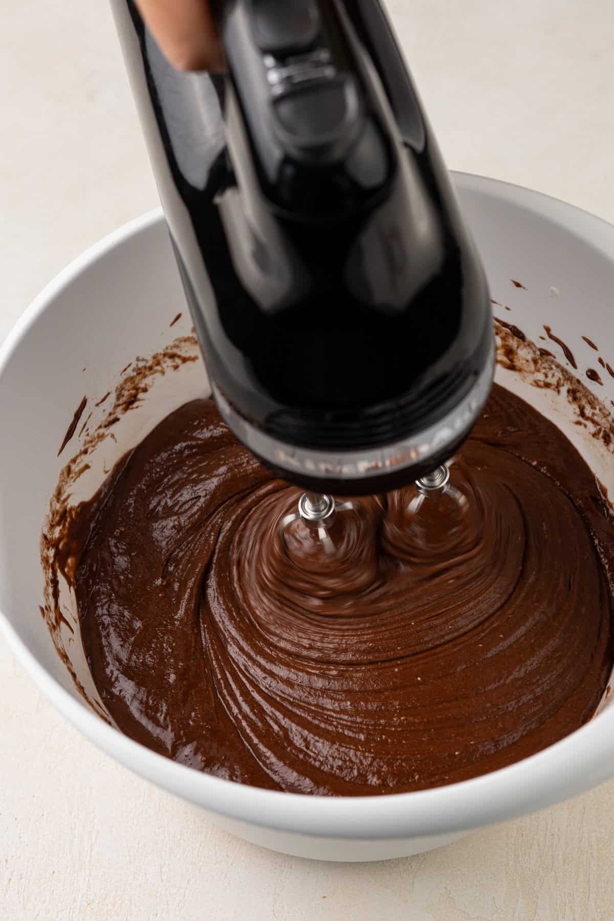 Hand mixer mixing doctored cake mix batter in a white bowl.