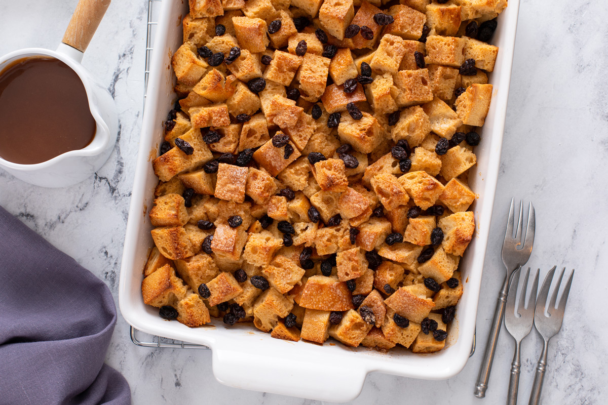 Overhead view of irish bread pudding in a white baking dish next to a pitcher of whiskey caramel sauce.