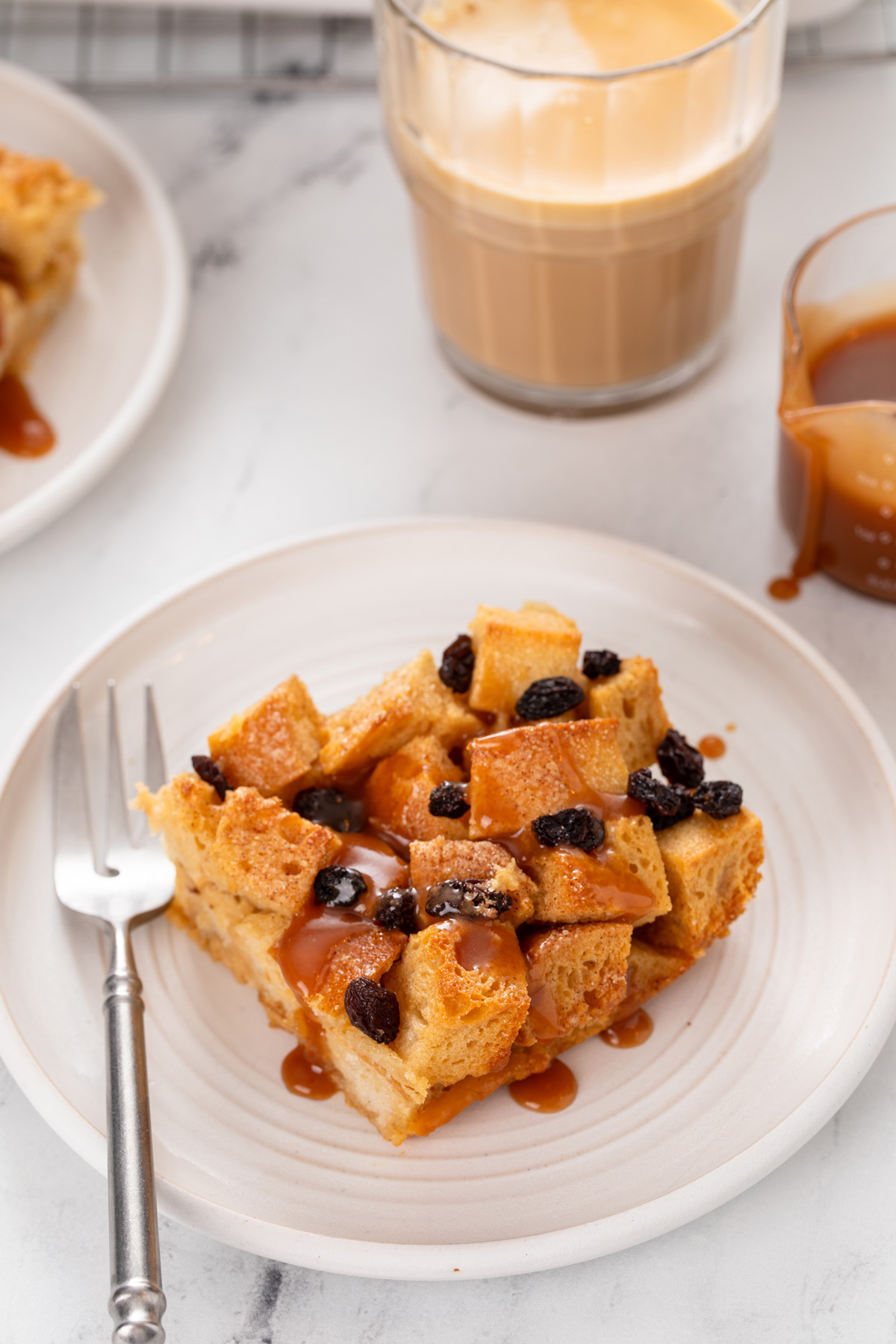 Slice of irish bread pudding topped with whiskey caramel sauce on a white plate.