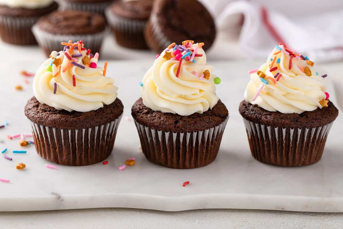 Three chocolate cupcakes topped with buttercream frosting lined up on a countertop.