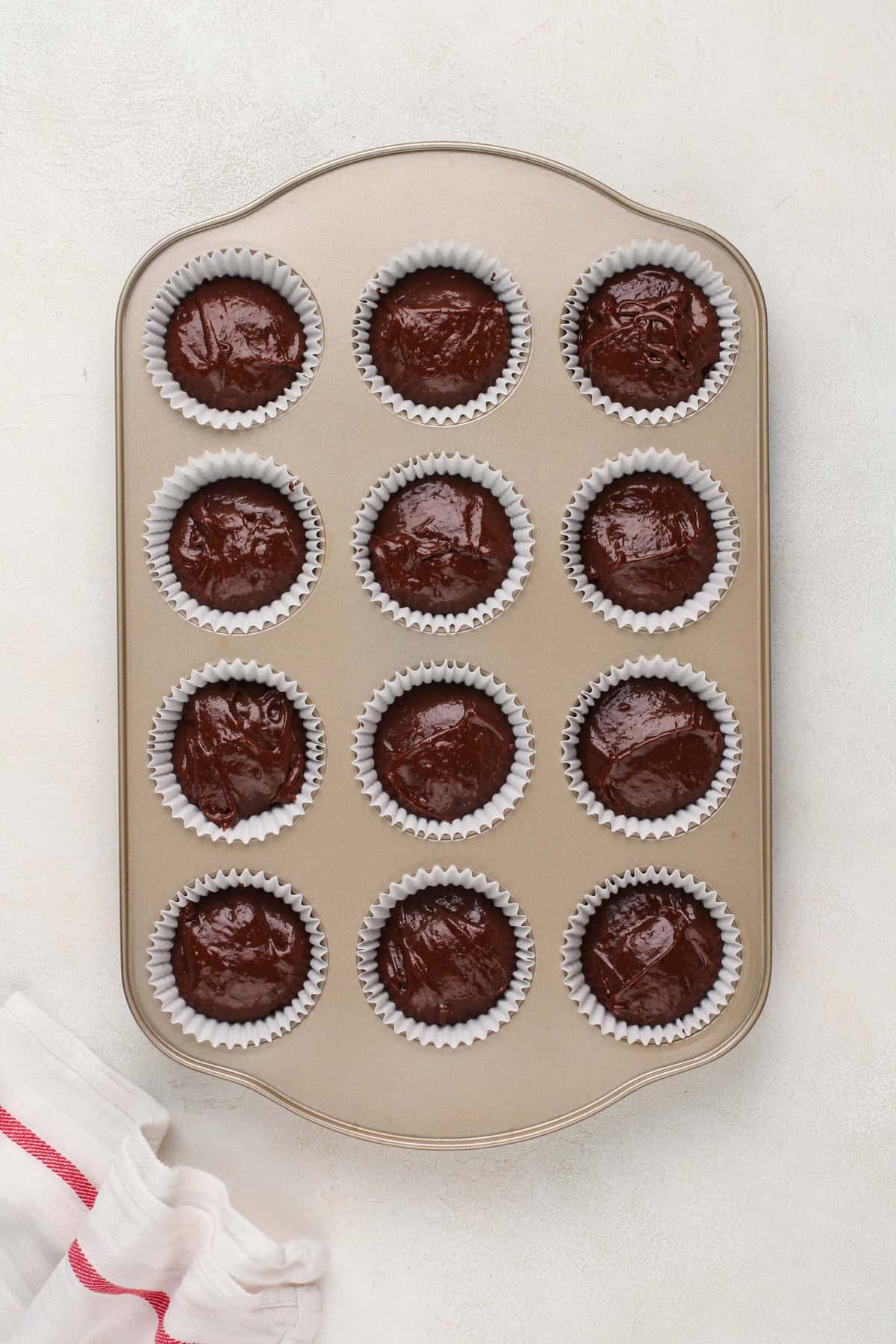 Unbaked chocolate cupcakes in a muffin tin, ready to go in the oven.