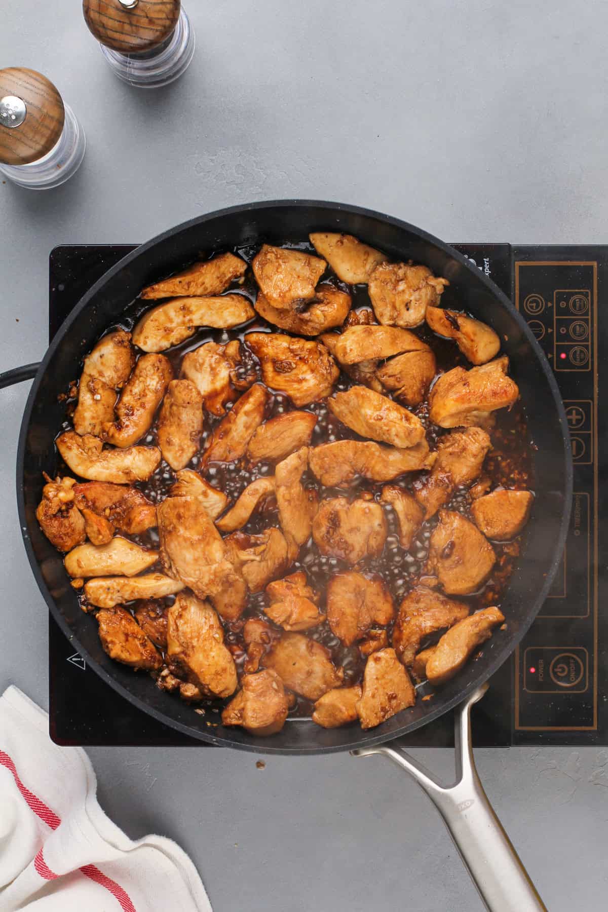 Chicken simmering in a honey soy sauce in a black skillet.