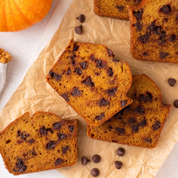 Slices of chocolate chip pumpkin bread scattered on a piece of parchment paper.