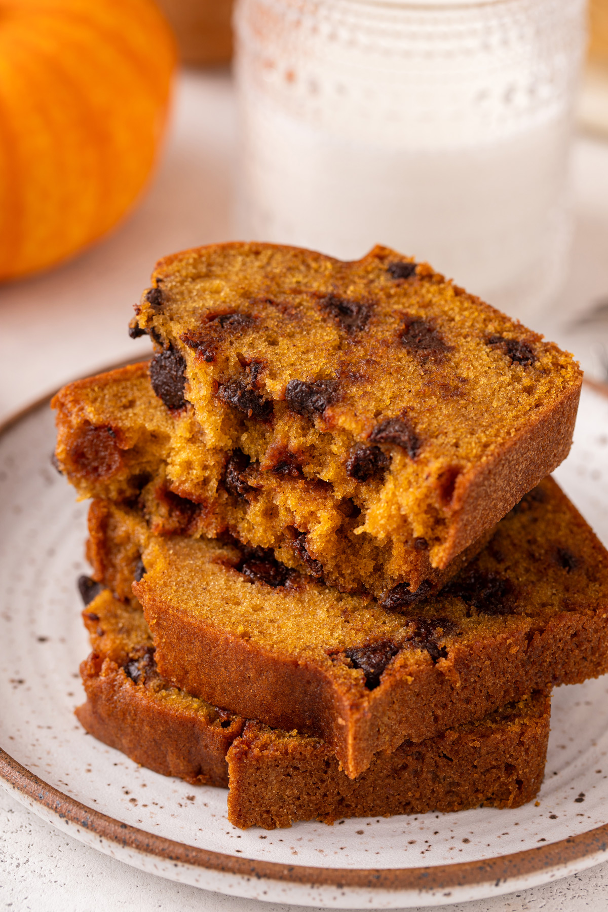 Slices of chocolate chip pumpkin bread stacked on a plate. The top slice is broken in half.