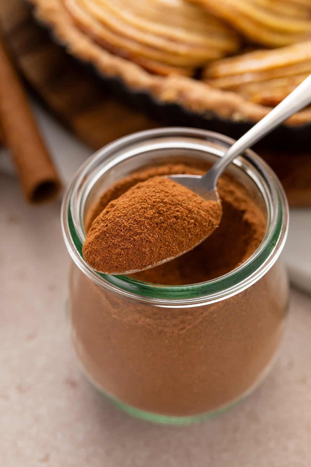 Spoon of apple pie spice perched on top of a jar of apple pie spice.