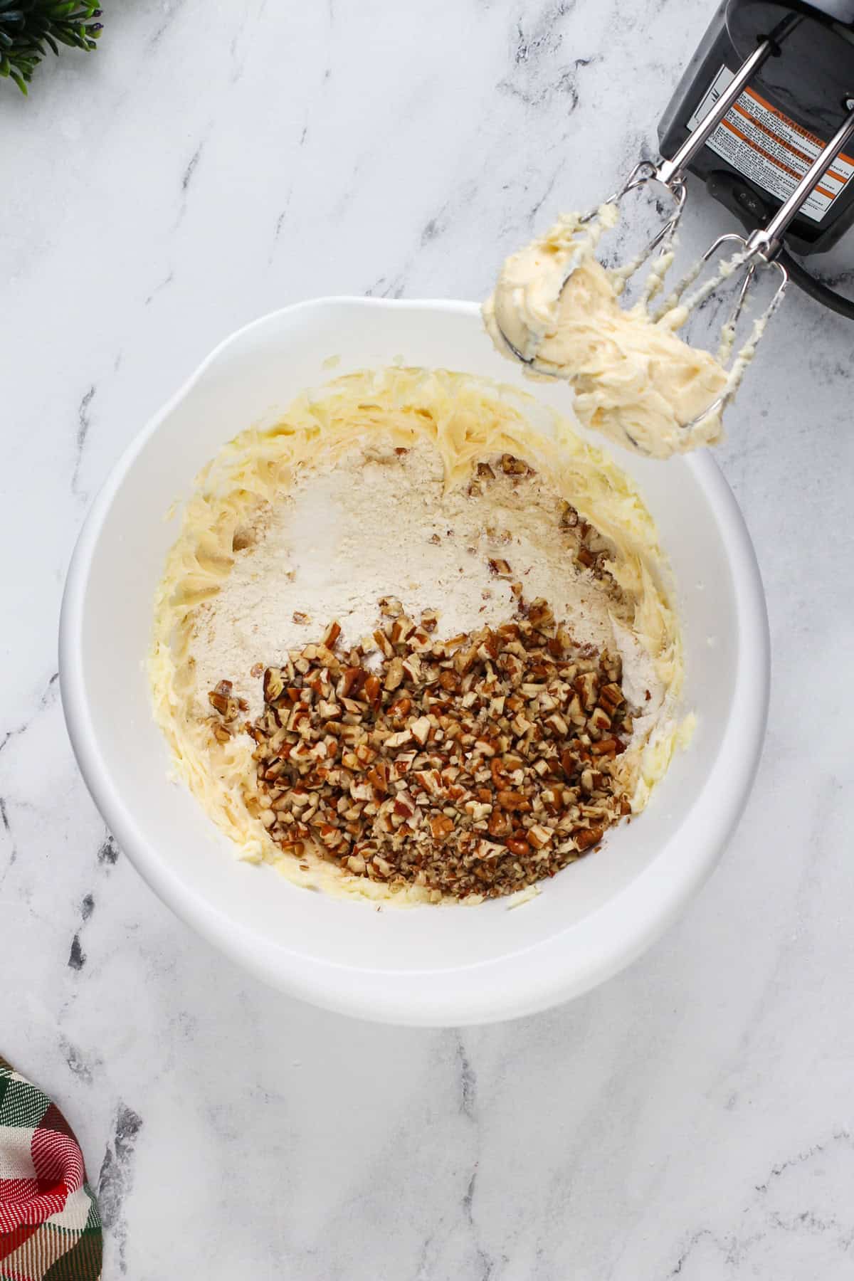 Dry ingredients and chopped pecans being added to creamed butter and sugar in a white bowl.