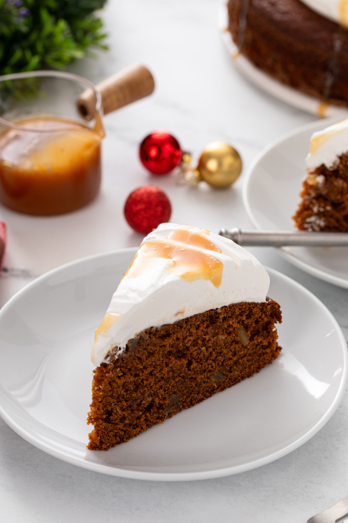 Slice of gingerbread cake topped with whipped cream and caramel sauce on a white plate.