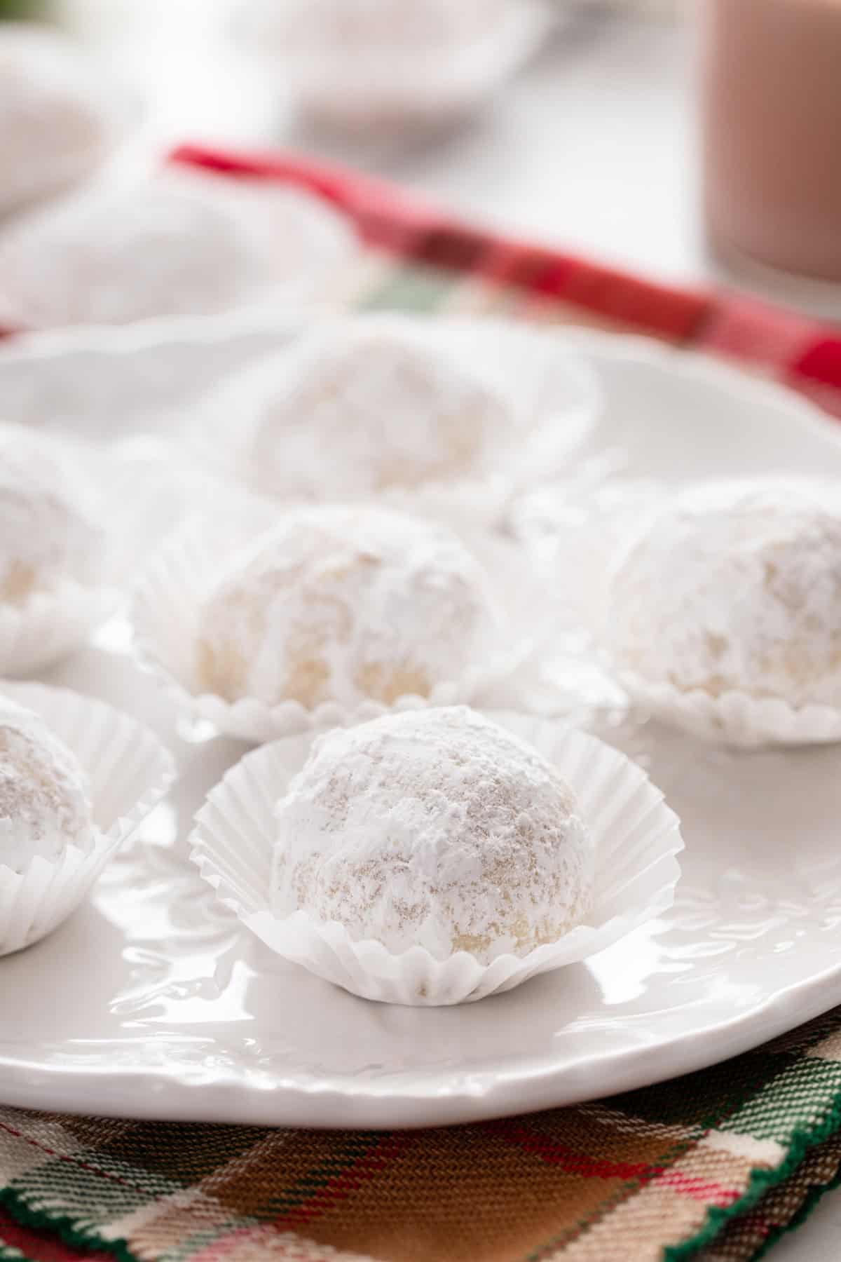 Close up of snowball cookies in mini cupcake liners on a white plate.