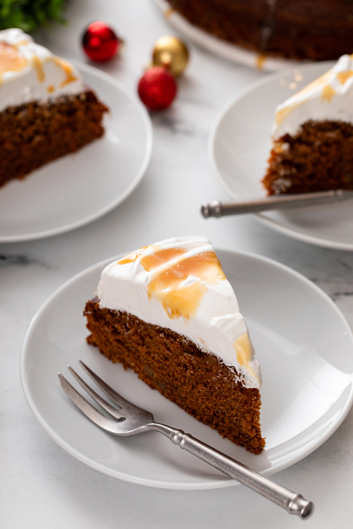 Slice of gingerbread cake next to a fork on a white plate.