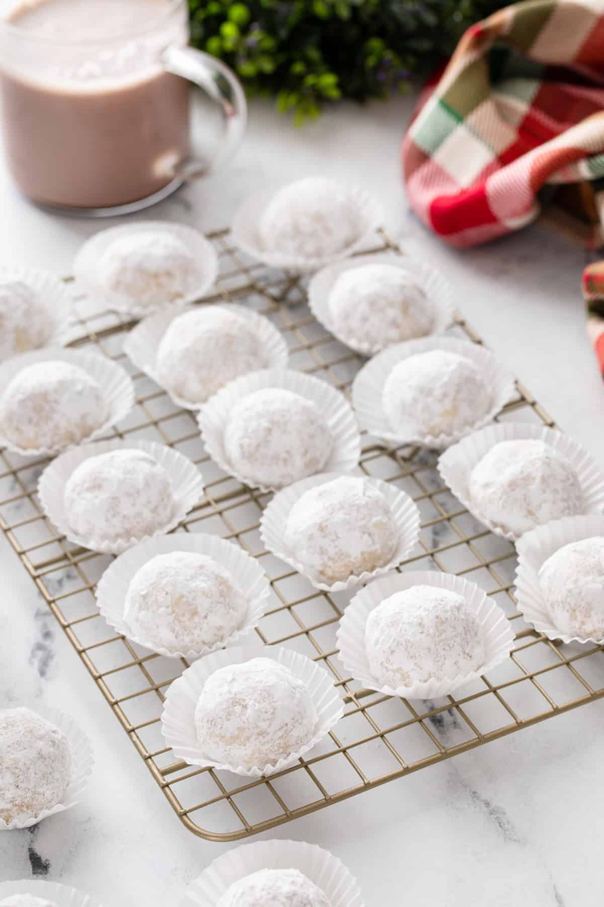 Snowball cookies in mini cupcake liners arranged on a wire rack.