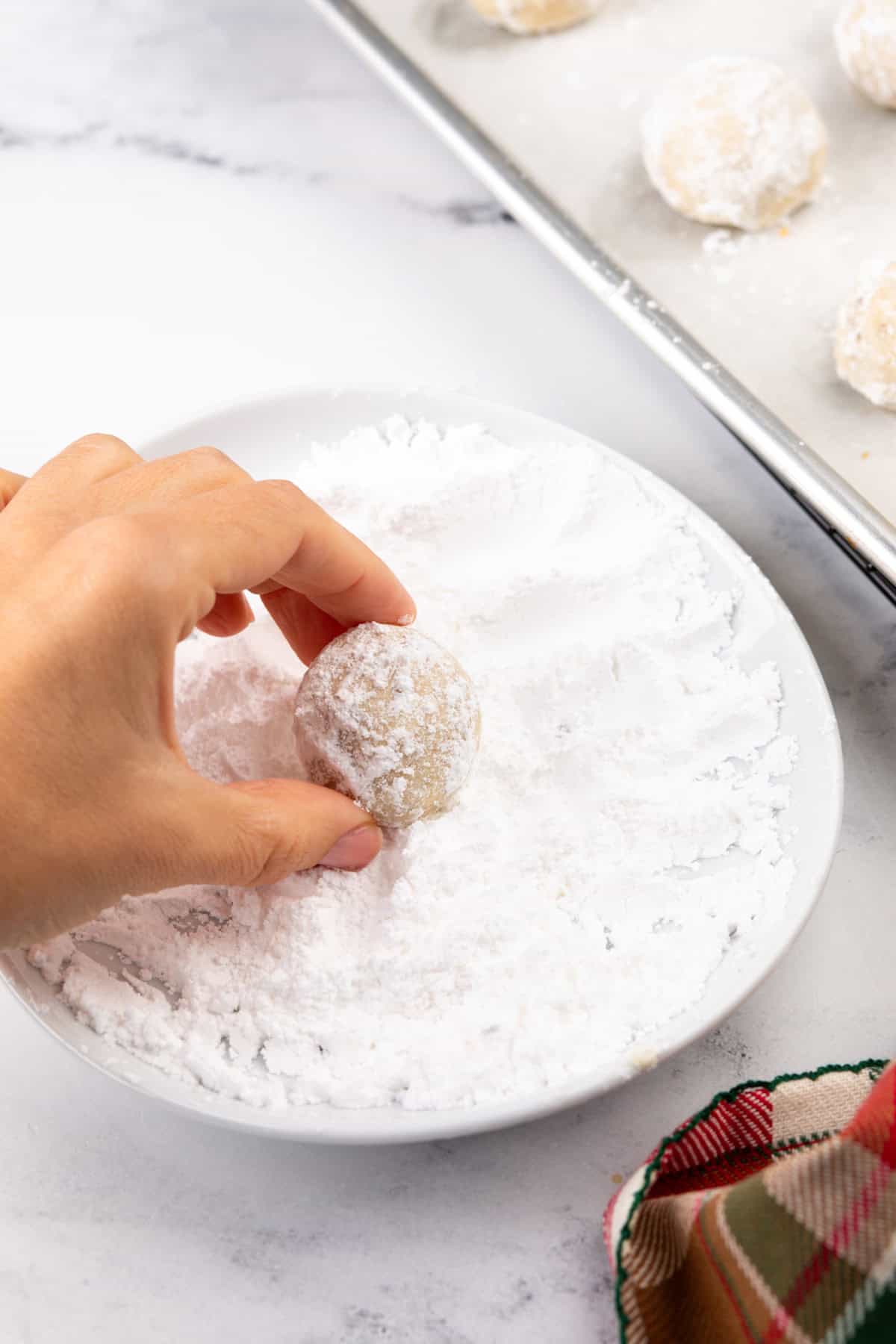 Hand rolling baked snowball cookie in powdered sugar.