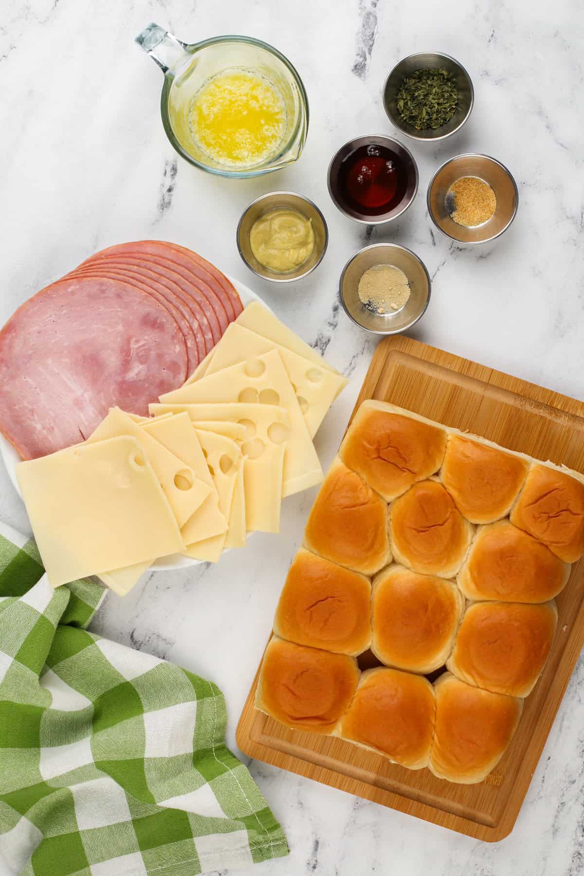 Ingredients for hot ham and cheese sliders arranged on a marble countertop.