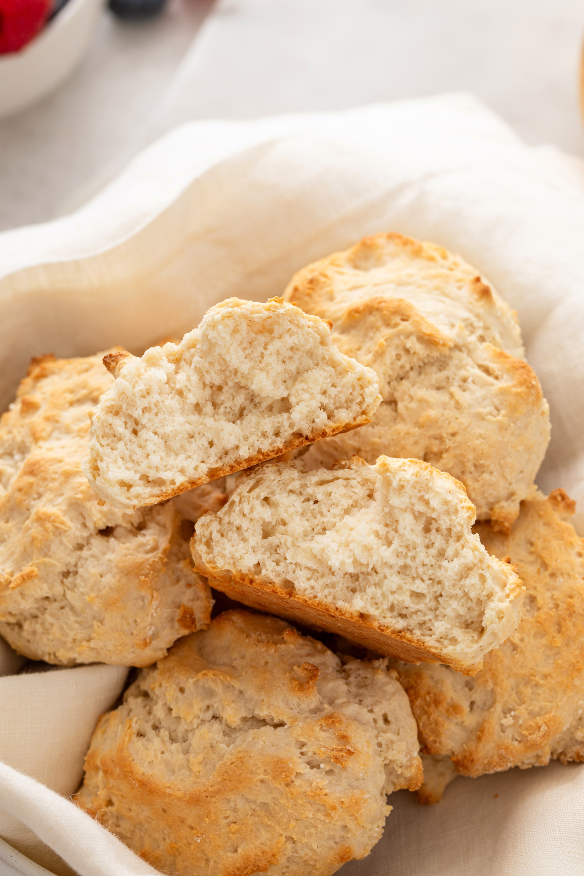 Halved bisquick biscuit resting on the top of a pile of biscuits in a bread basket.