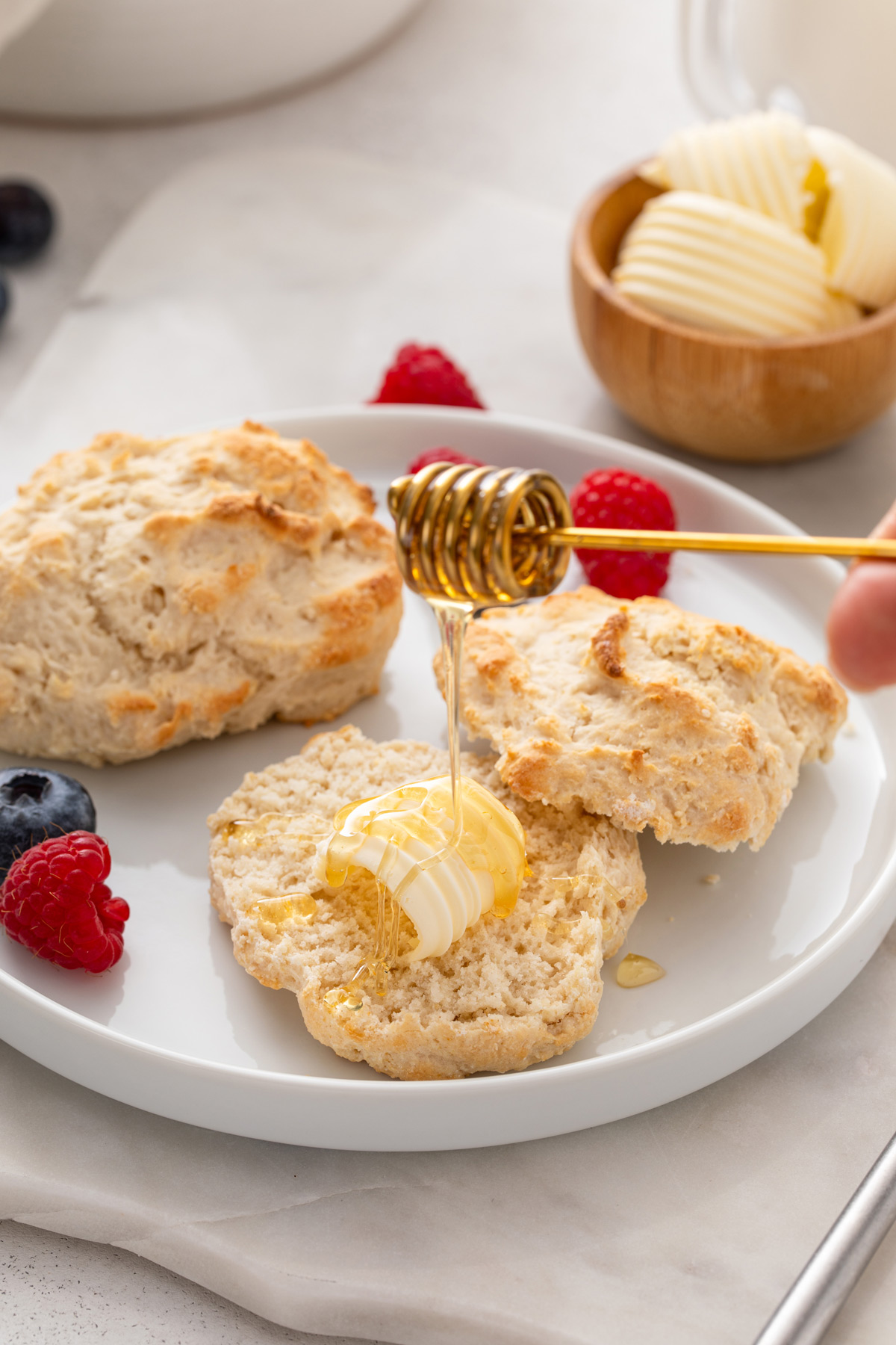 Honey being drizzled over a buttered bisquick biscuit on a white plate.