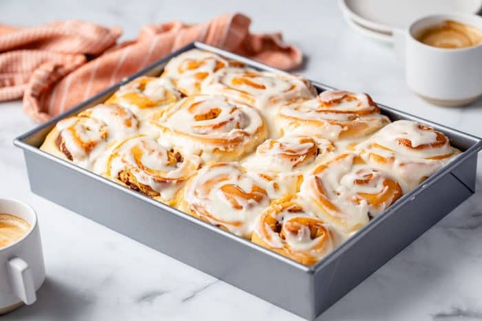 Pan of baked and frosted pumpkin spice cinnamon rolls on a countertop next to a dish towel