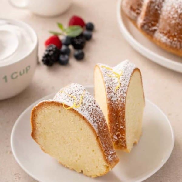 Two slices of cream cheese pound cake dusted with powdered sugar on a white plate.