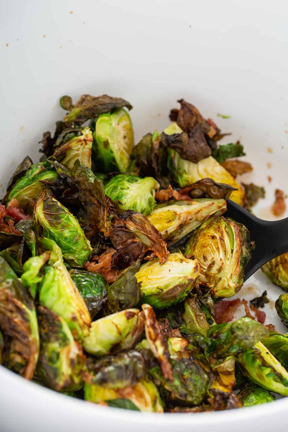 Freshly air fried brussels sprouts tossed with bacon in a white mixing bowl