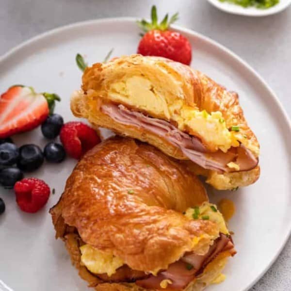 White plate topped with a halved croissant breakfast sandwich and fresh berries.