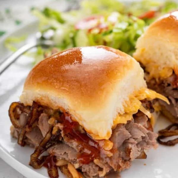 Close up of cheesy roast beef slider on a white plate.