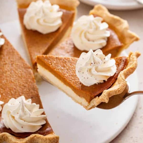 Pie server lifting up a slice of pumpkin cream cheese pie from a white platter.