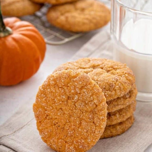 Four pumpkin snickerdoodles stacked on a cloth napkin with a fifth cookie leaning against the stack.