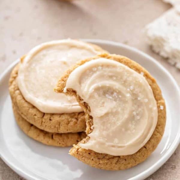 Two stacked maple cookies on a white plate with a third cookie leaning against the stack. A bite has been taken from the third cookie.