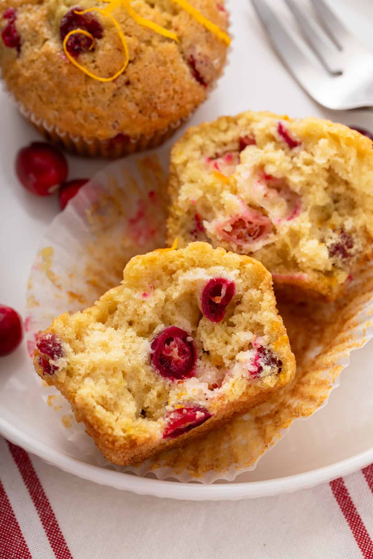 Cranberry orange muffin cut in half on a white plate next to a whole muffin.