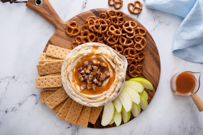 Overhead view of a bowl of snickers dip surrounded by various dippers on a wooden board.