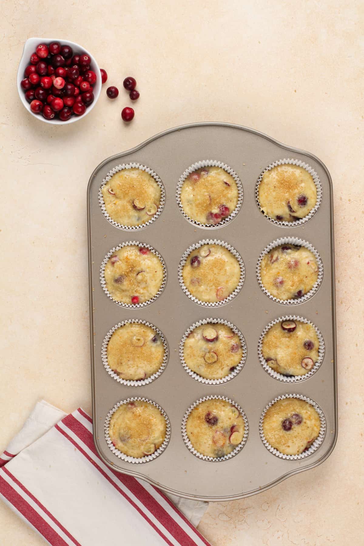 Unbaked orange and cranberry muffins in a muffin tin, ready to bake.