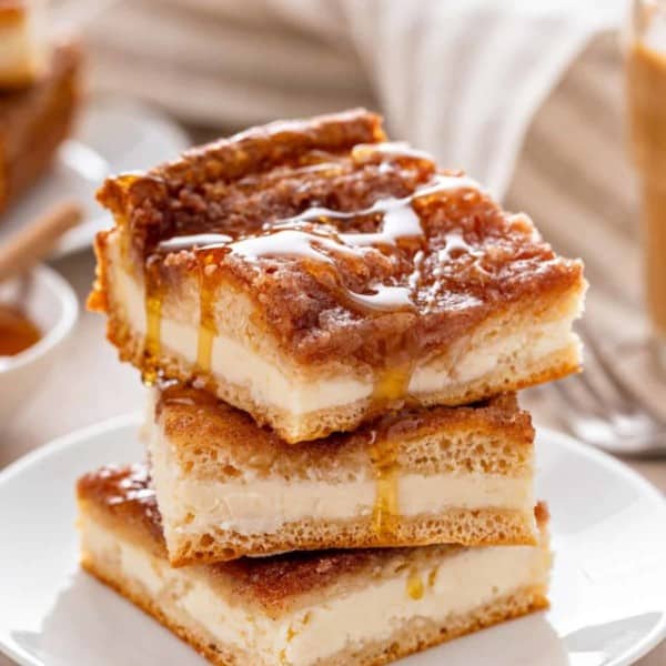 Three slices of sopapilla cheesecake stacked on a white plate, with honey drizzled on top.