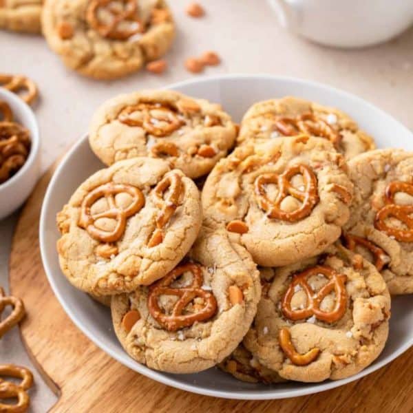 Several salted caramel pretzel cookies on a large plate set on a wooden board.