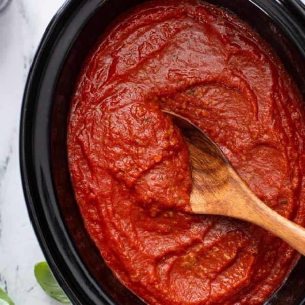 Wooden spoon stirring pureed spaghetti sauce in a slow cooker.