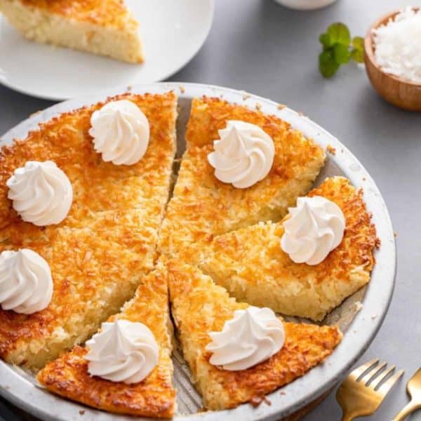 Sliced impossible coconut pie garnished with whipped cream in a pie plate.