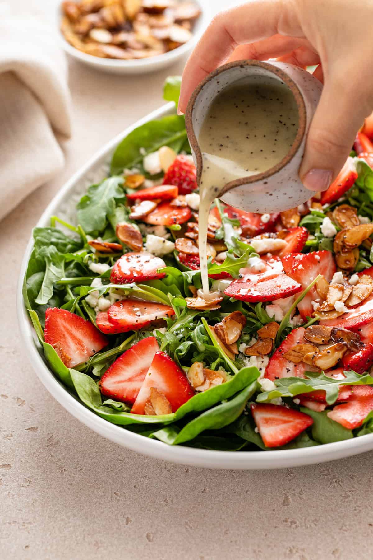 Poppy seed dressing being poured over strawberry salad in a serving bowl.